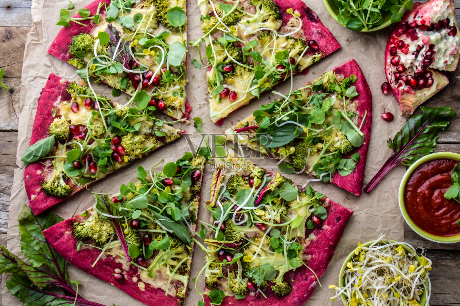 切成粉红色的甜菜根面团披萨，配上蔬菜、奶酪、新鲜的叶子、芽和石榴照片摄影图片
