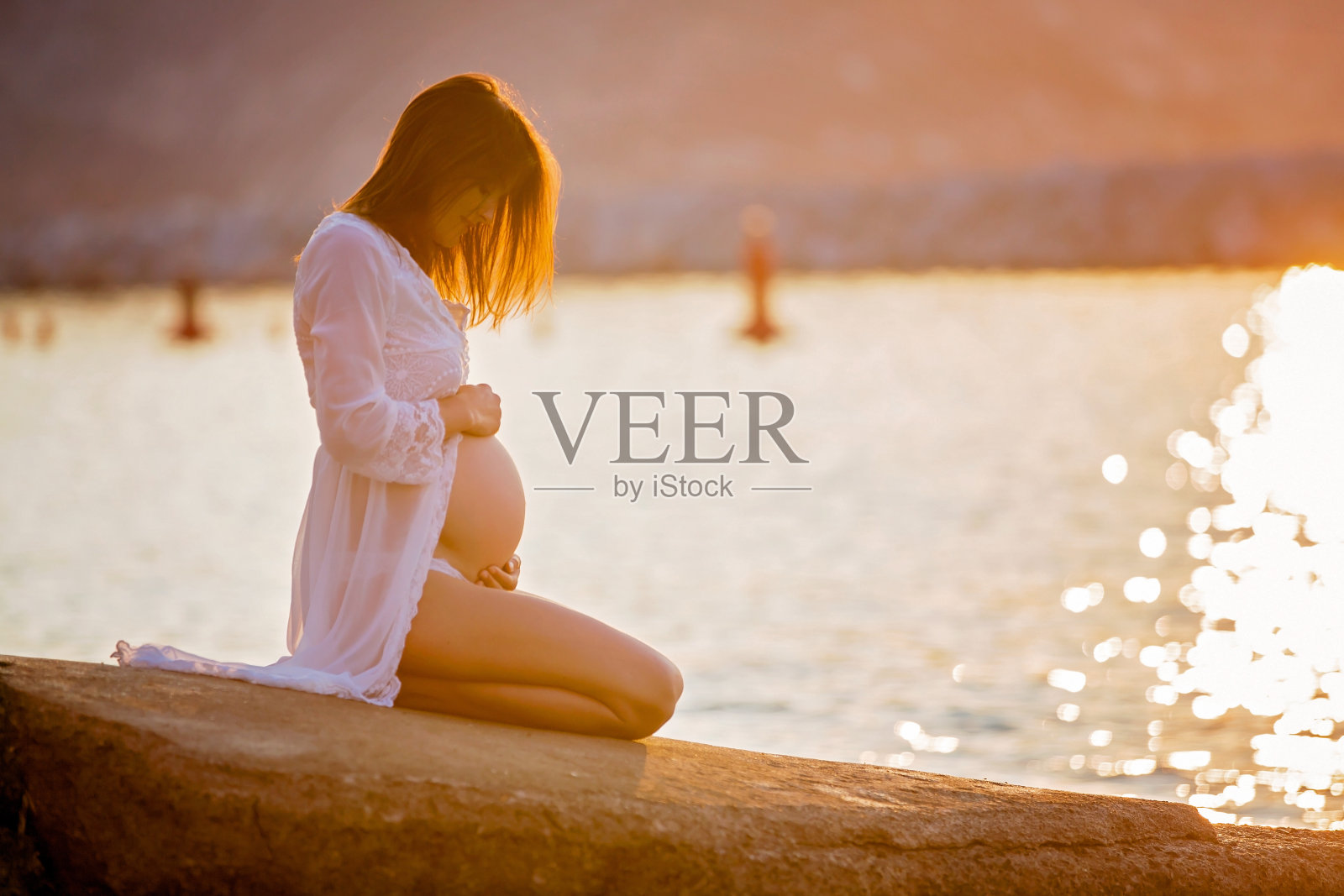 美丽的孕妇，坐在沙滩上的日出，华丽的白色长袍照片摄影图片