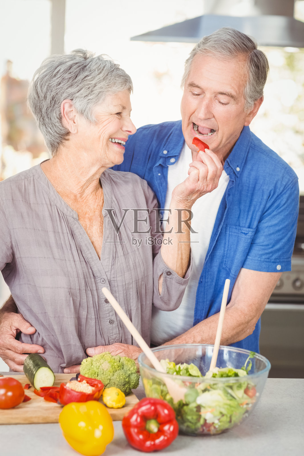 快乐的老妇人一边站在柜台边喂丈夫照片摄影图片