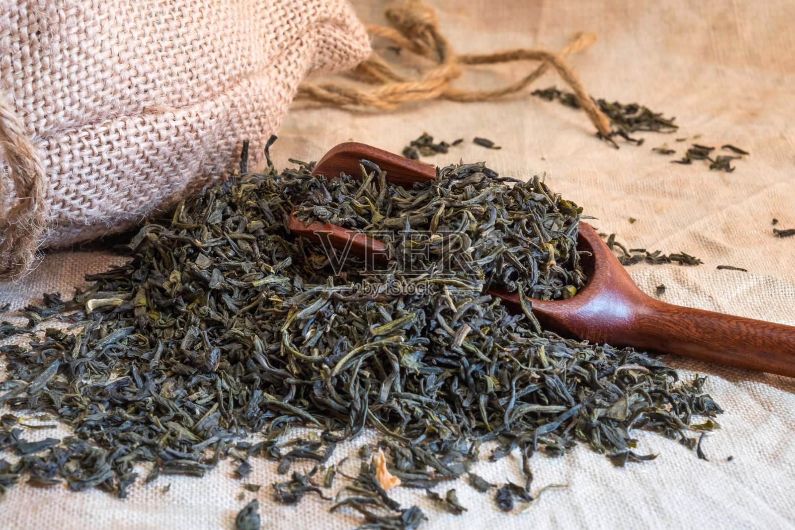 在灰色亚麻桌布上，阳光下用麻袋吸竹勺的中国绿茶叶子。照片摄影图片