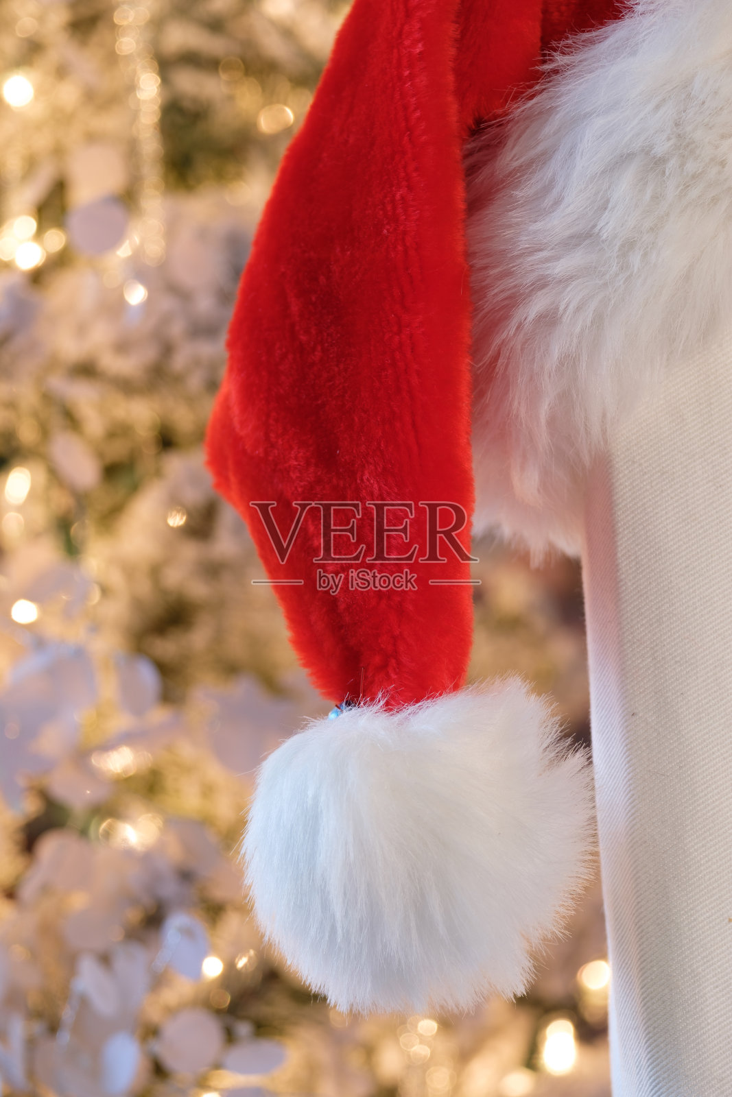 红色和白色的圣诞帽，背景是点亮的节日树的温暖灯光照片摄影图片