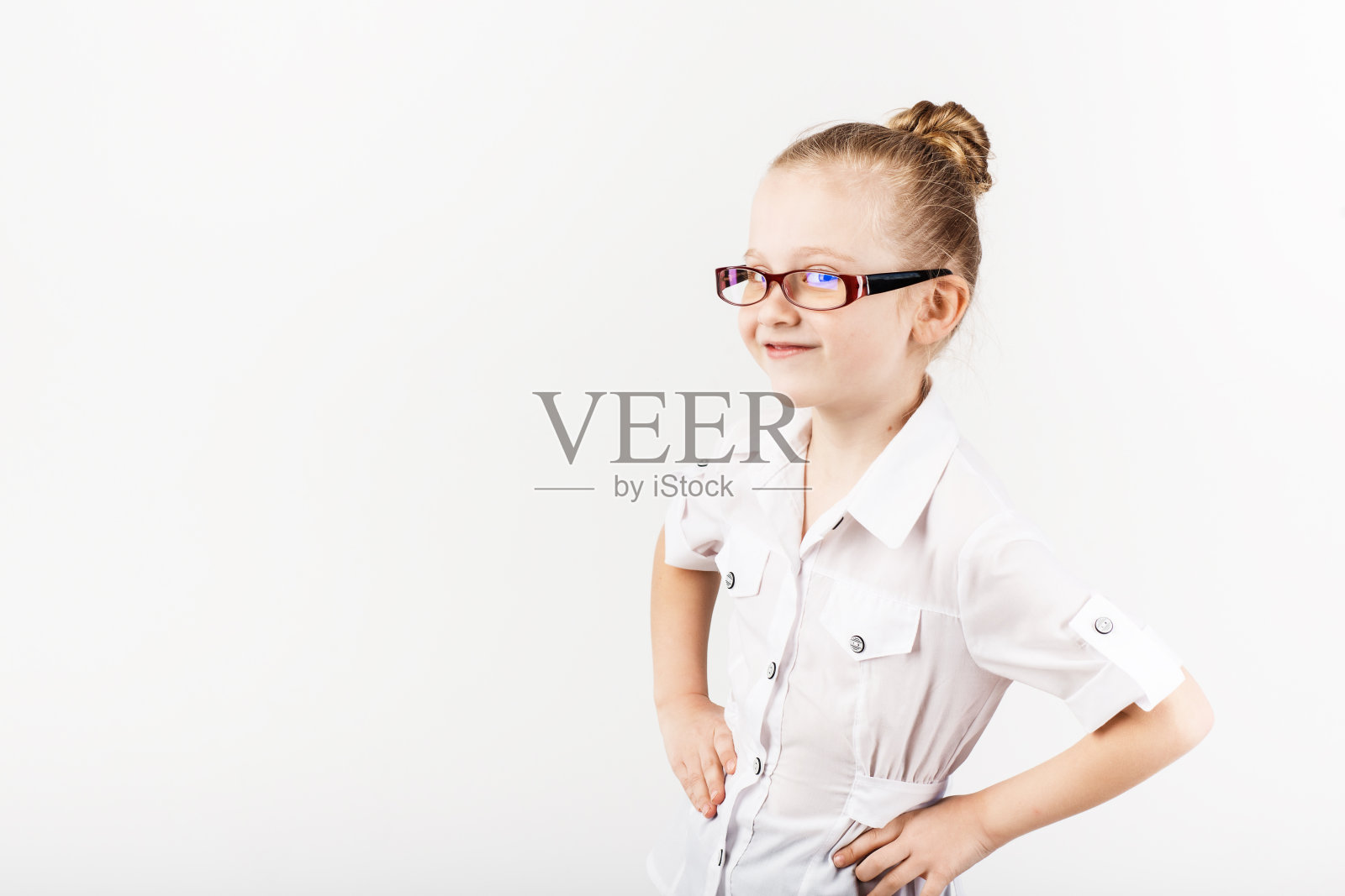 有趣的小女孩戴着眼镜，在白色背景下模仿严厉的老师。拿着书的小学生。看相机。学校的概念。照片摄影图片