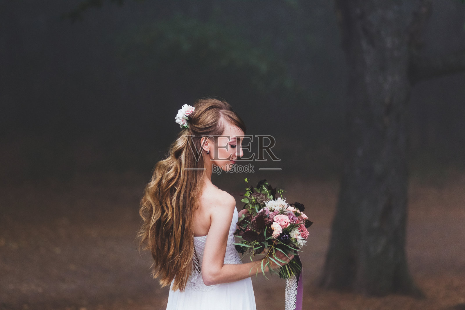 年轻时髦的新娘手拿粉色和黑色的婚礼花束。周围的森林照片摄影图片