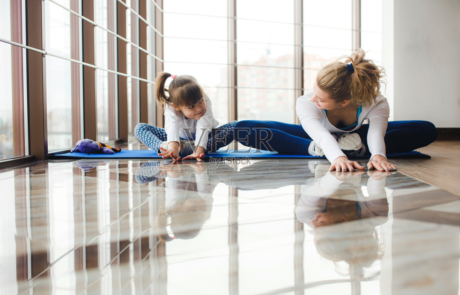 母亲和女儿在健身房的瑜伽垫上伸展照片摄影图片
