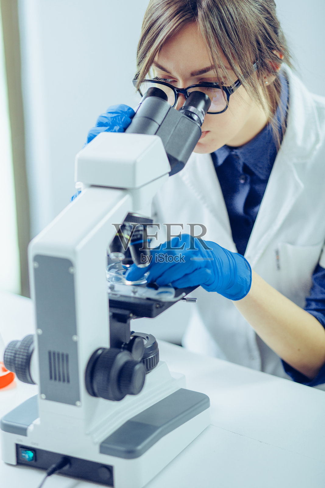 在实验室里透过显微镜观察的年轻科学家。年轻的科学家正在做一些研究。照片摄影图片
