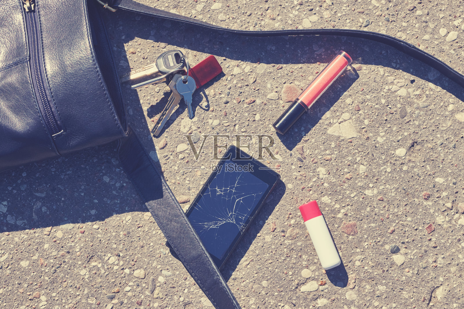 手提包，坏掉的手机，钥匙和口红在柏油路上。照片摄影图片