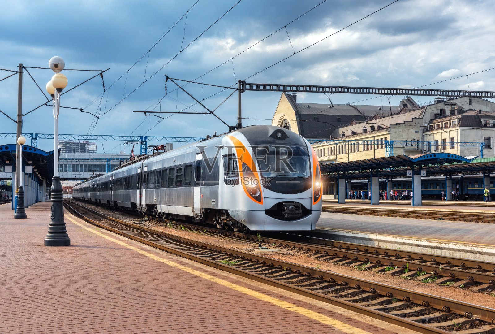 美丽的火车在火车站日落在欧洲。火车站站台上的现代城际列车。城市风景与美丽的客运列车在铁路和建筑物。铁路运输照片摄影图片