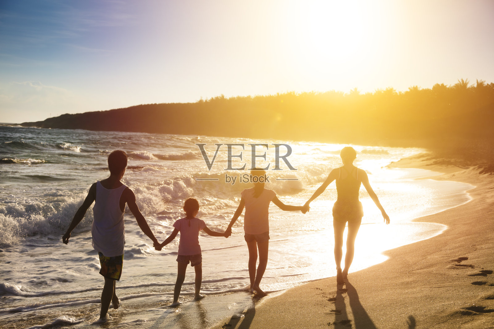 日落时分，幸福的年轻家庭在海滩上散步照片摄影图片