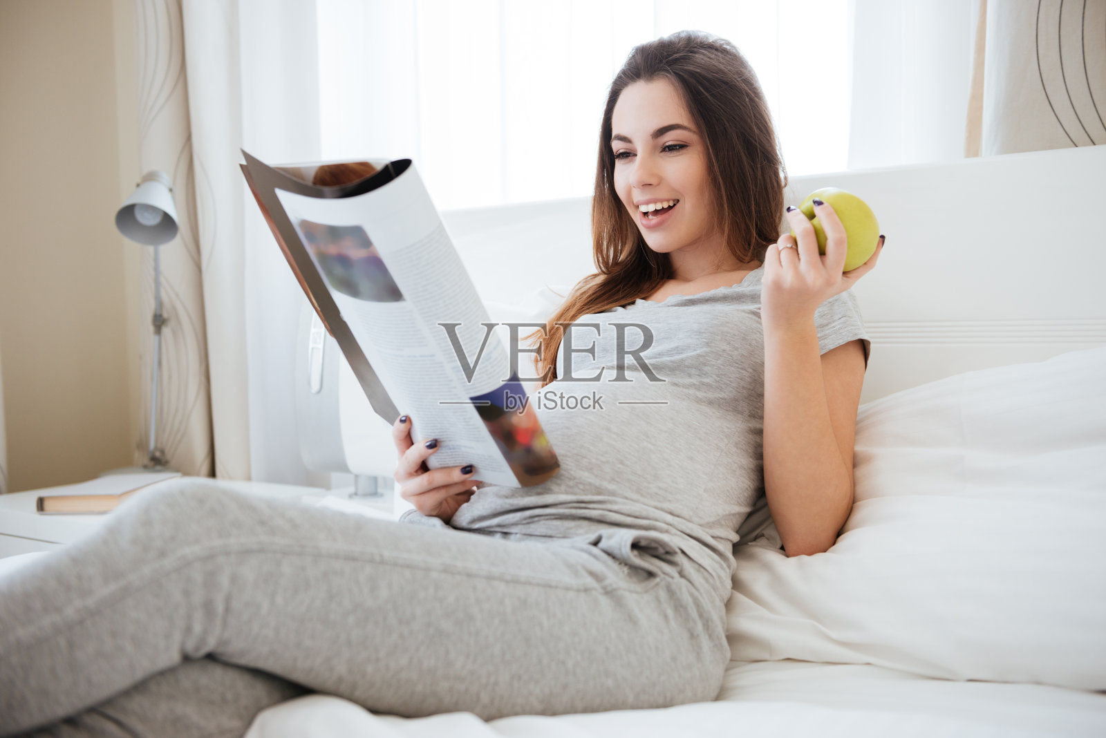 快活的孕妇在床上吃苹果看杂志照片摄影图片