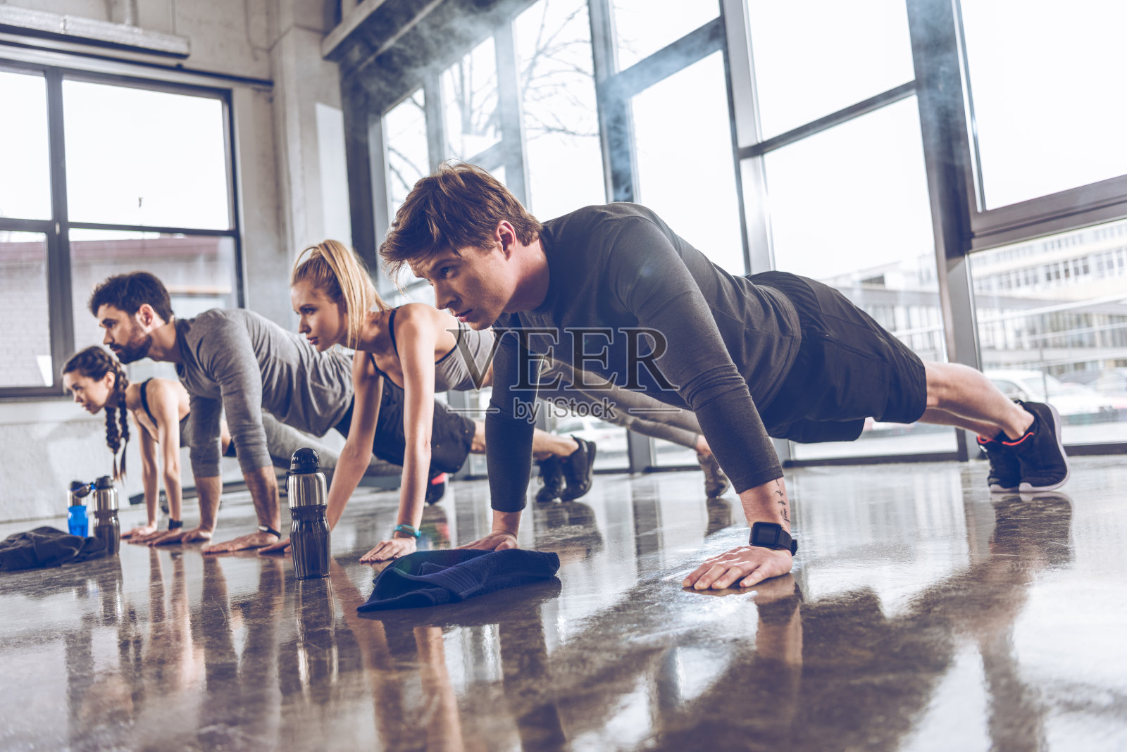 一群运动的年轻人穿着运动服在健身房做俯卧撑或平板支撑，团体健身概念照片摄影图片