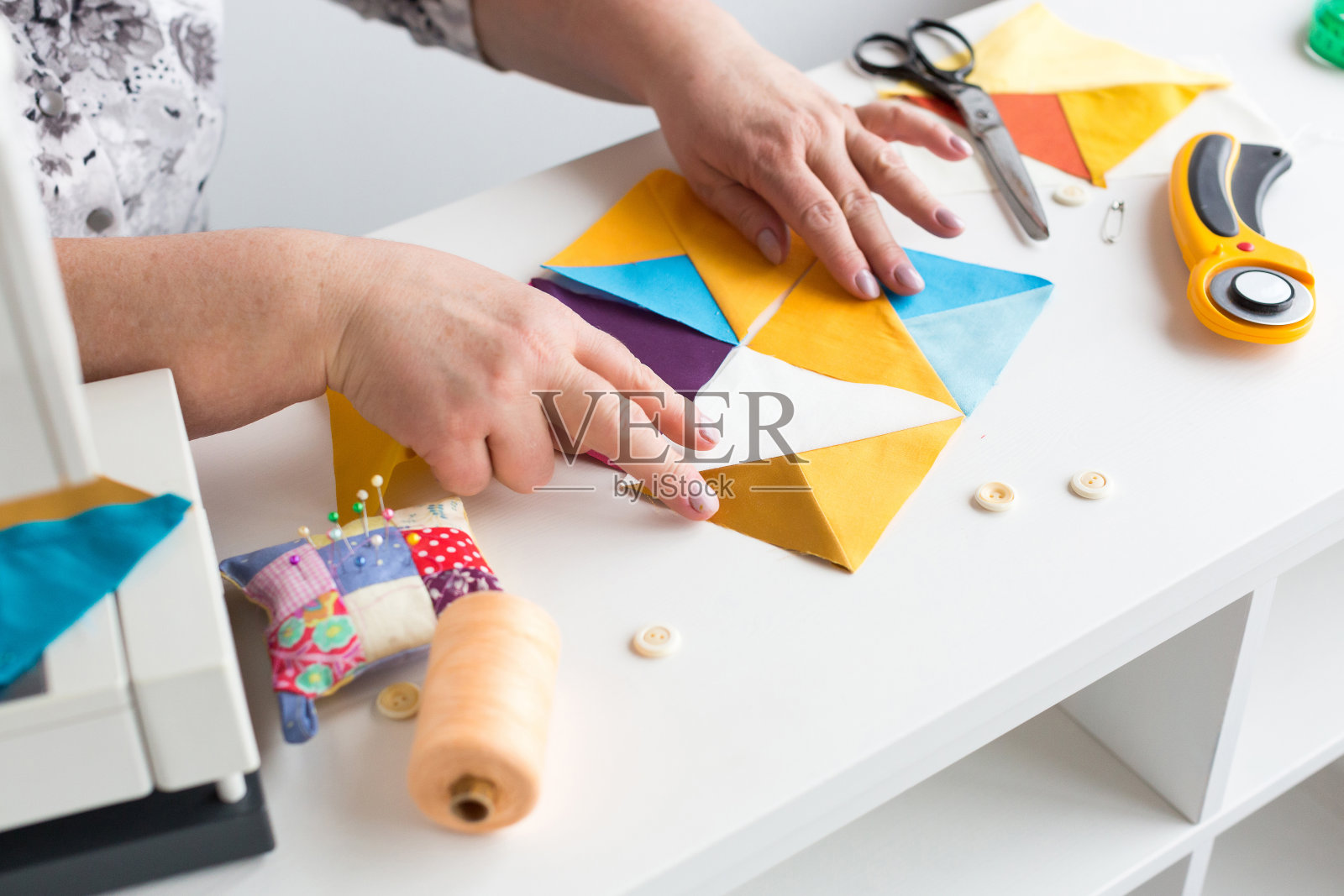 缝纫手工绗缝在车间的一个裁缝女人在白色的背景上-裁缝的手收集从桌面的彩色织物碎片在缝纫机上拼接照片摄影图片