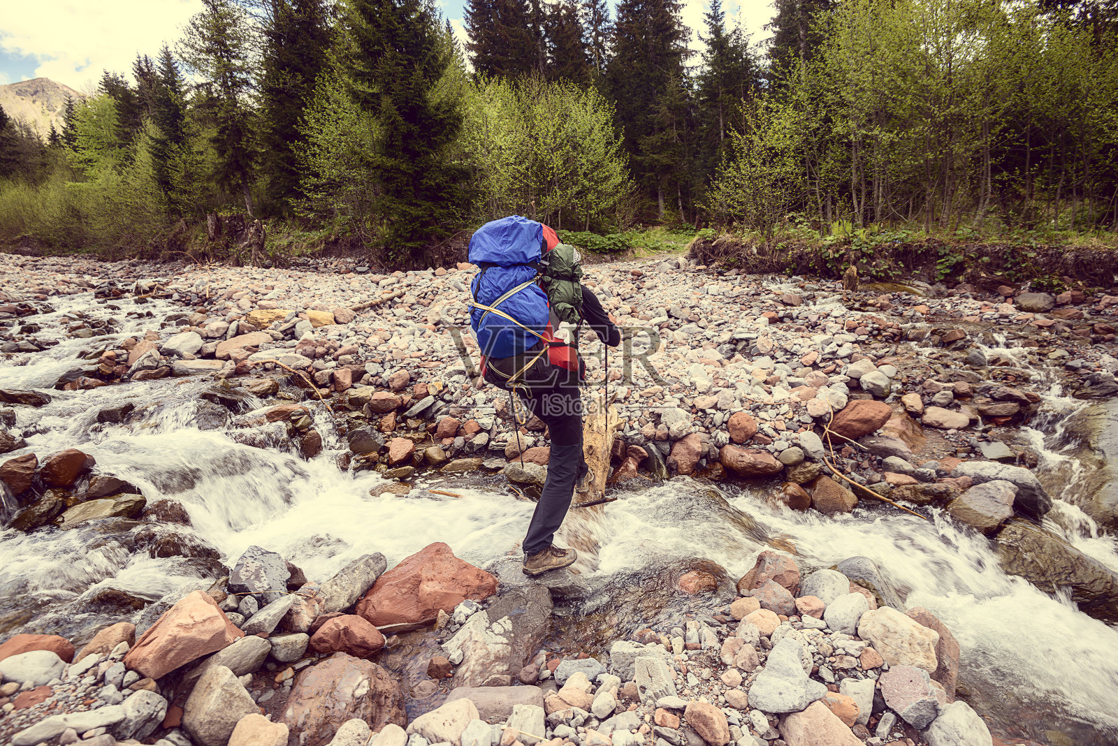 一名背着背包的男子穿过一条山间河流。的形象照片摄影图片