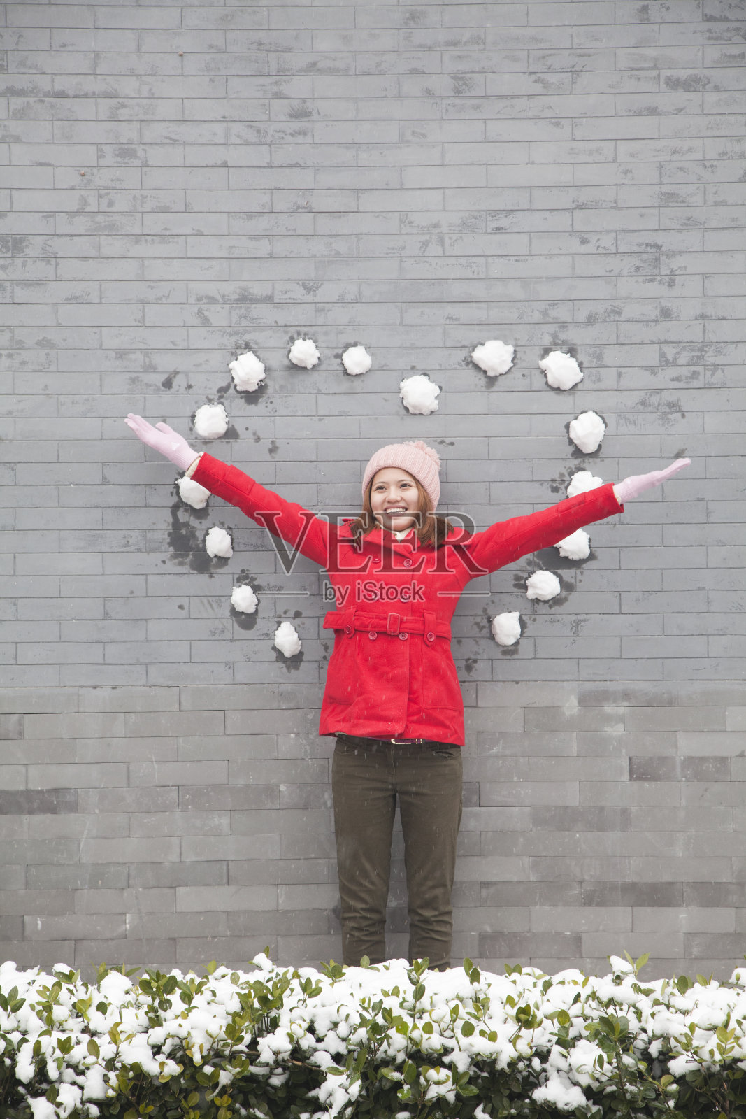年轻女子站在墙上，手里拿着心形的雪球照片摄影图片