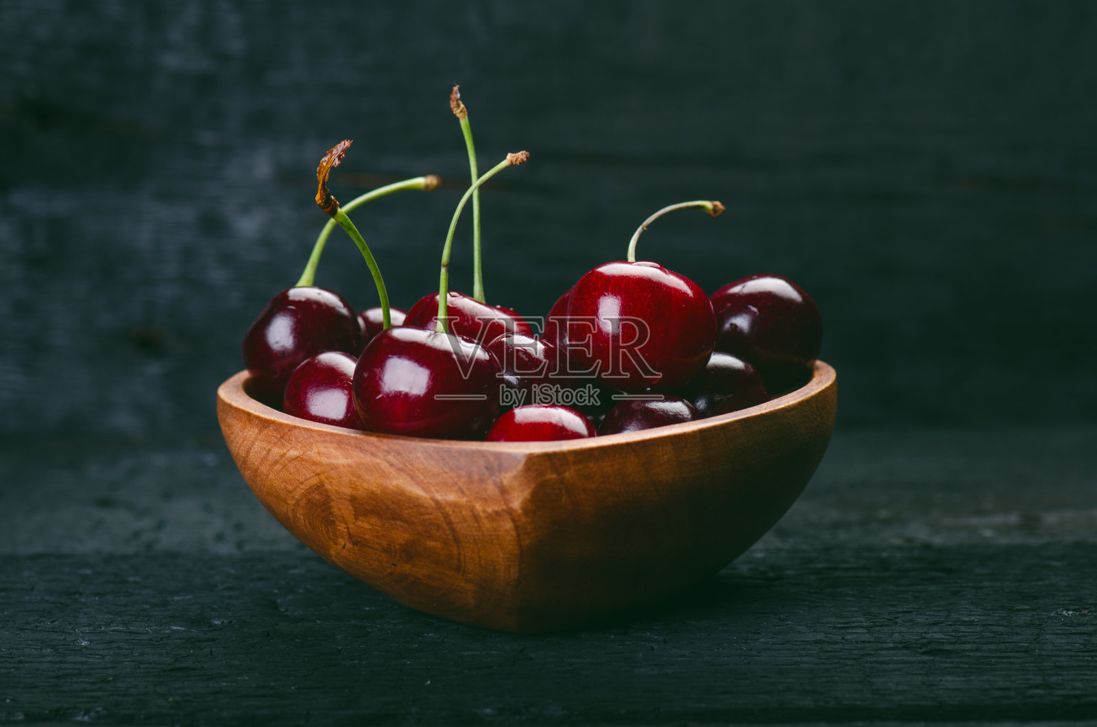 把樱桃放在木碗里，做成心形。天然木烧桌。新鲜食品的概念。水果。夏天的时间照片摄影图片