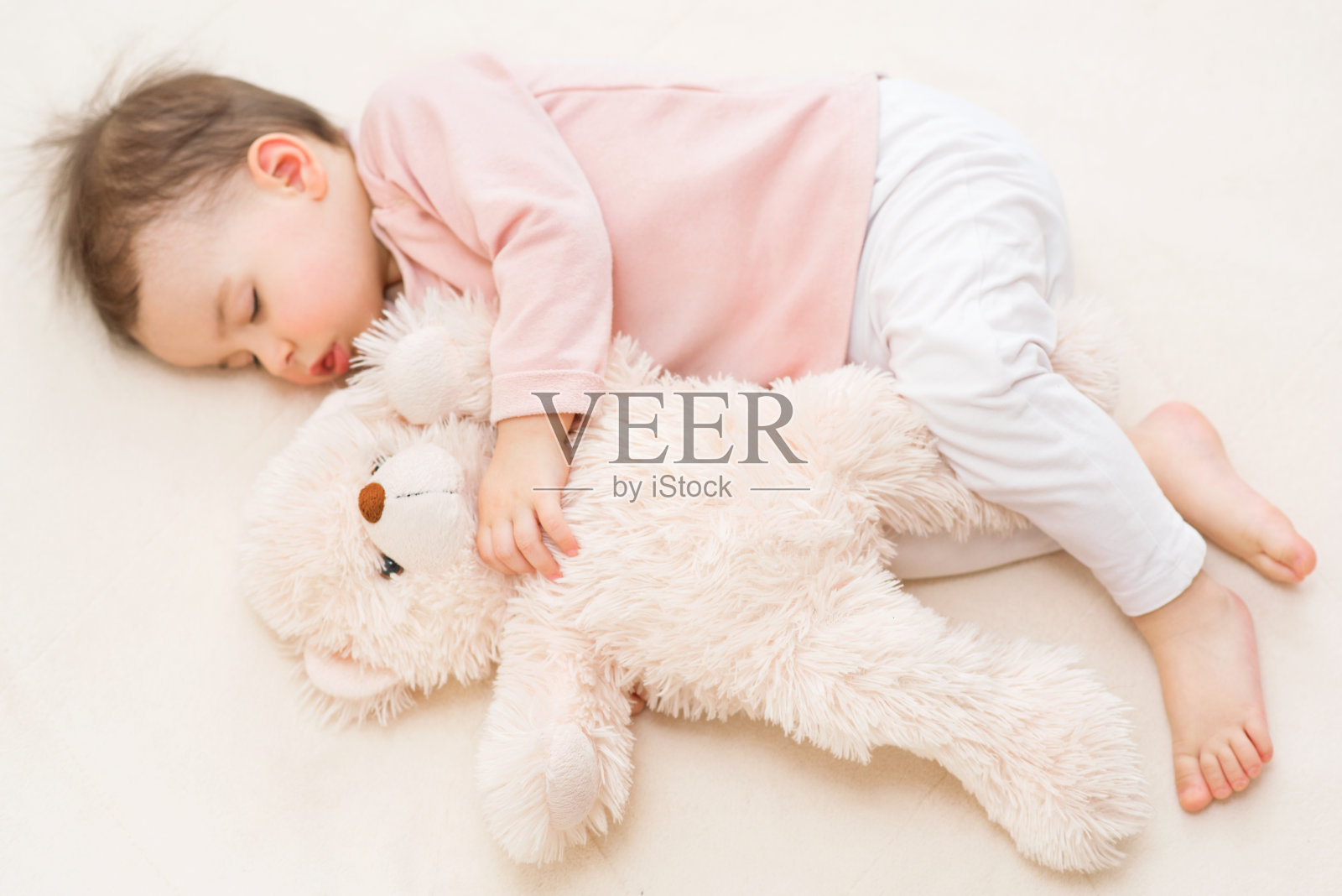 漂亮的蹒跚学步的小女孩正在睡觉，床上放着一只毛茸茸的泰迪熊照片摄影图片