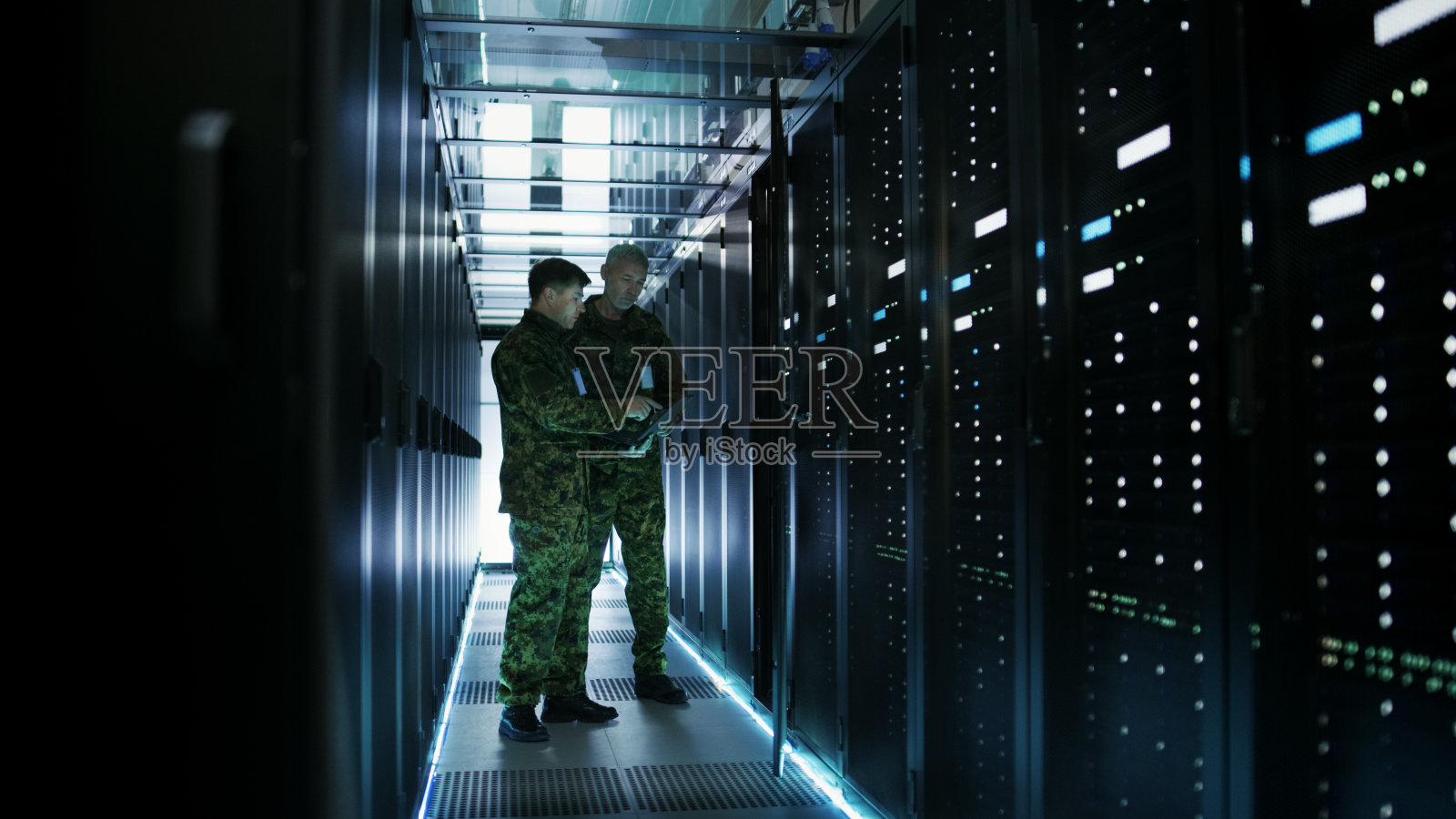 在数据中心，两名军人使用开放式服务器机架机柜工作。一个是军用版笔记本电脑。照片摄影图片