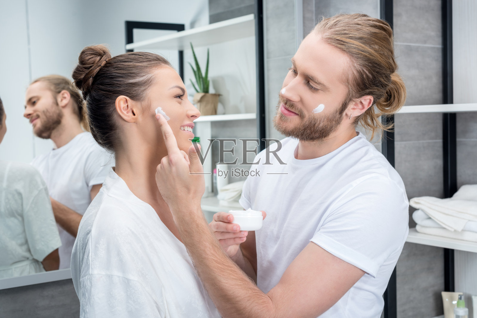年轻的胡子丈夫在浴室里给妻子的脸颊涂面霜照片摄影图片
