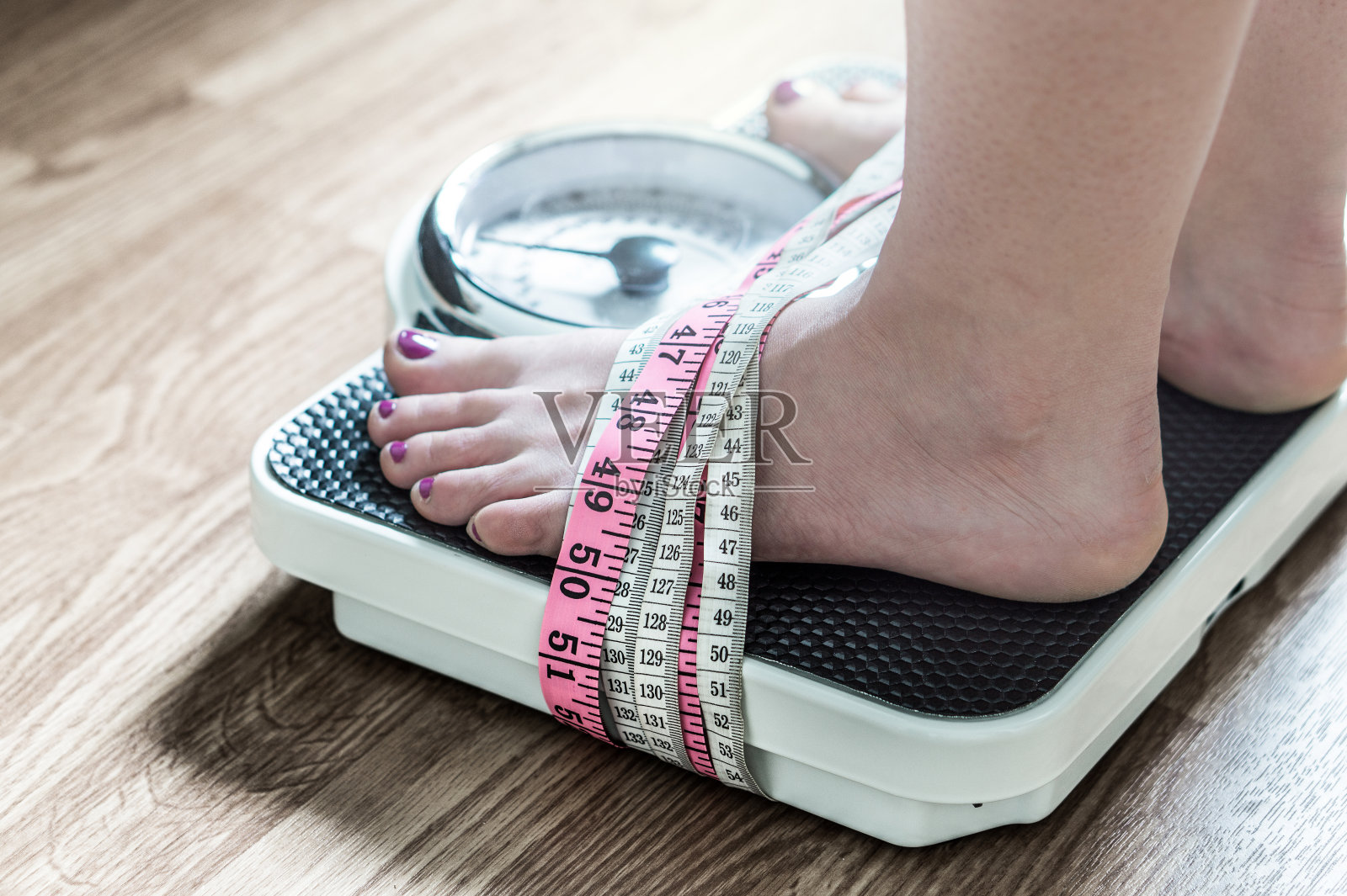 双脚用卷尺绑在秤上。对减肥上瘾和痴迷。厌食症和饮食失调的概念。照片摄影图片