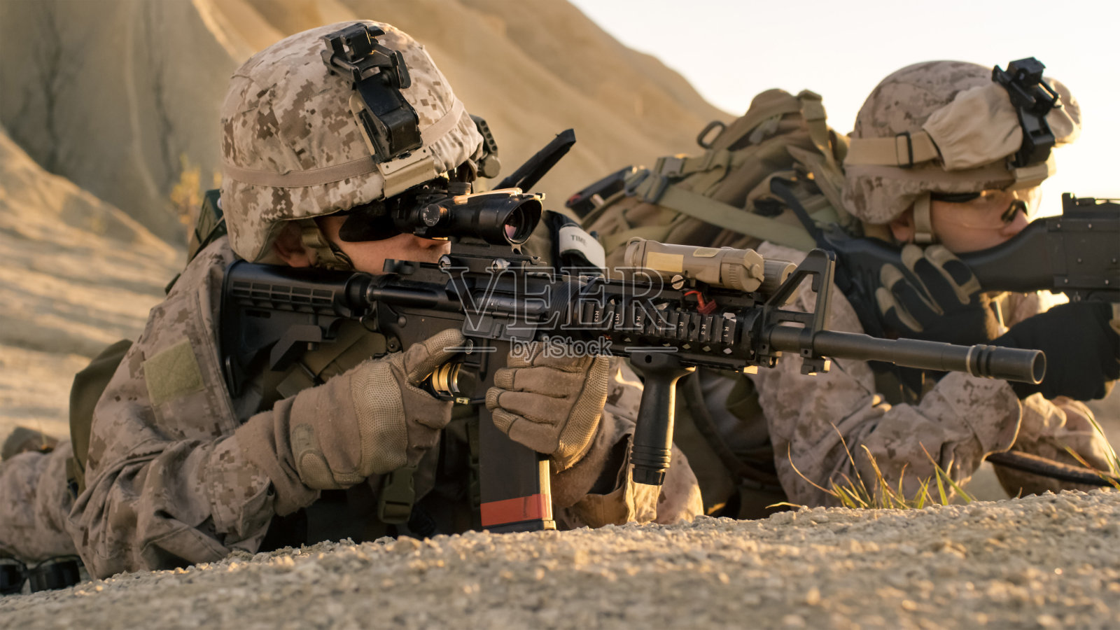 在沙漠环境中，士兵躺在山上，用突击步枪瞄准。照片摄影图片