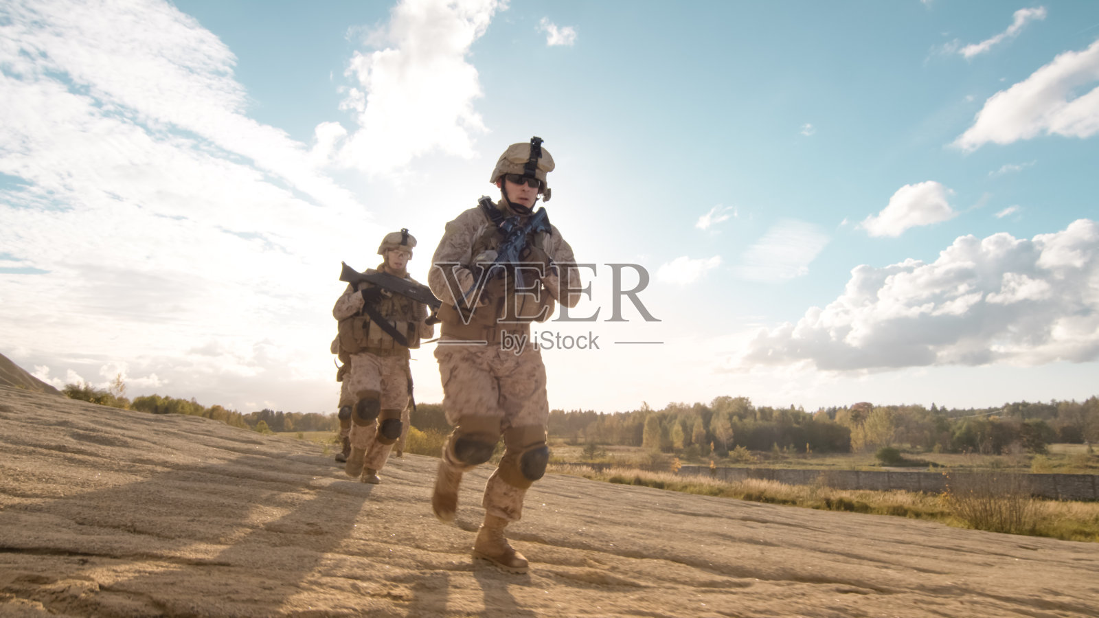 一小队全副武装的士兵在沙漠中以单列纵队行进。照片摄影图片