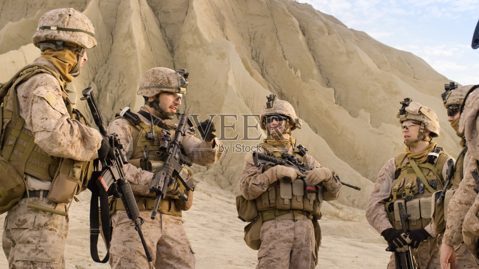 一群全副武装的士兵在沙漠军事行动前站成一圈并计划他们的行动。照片摄影图片