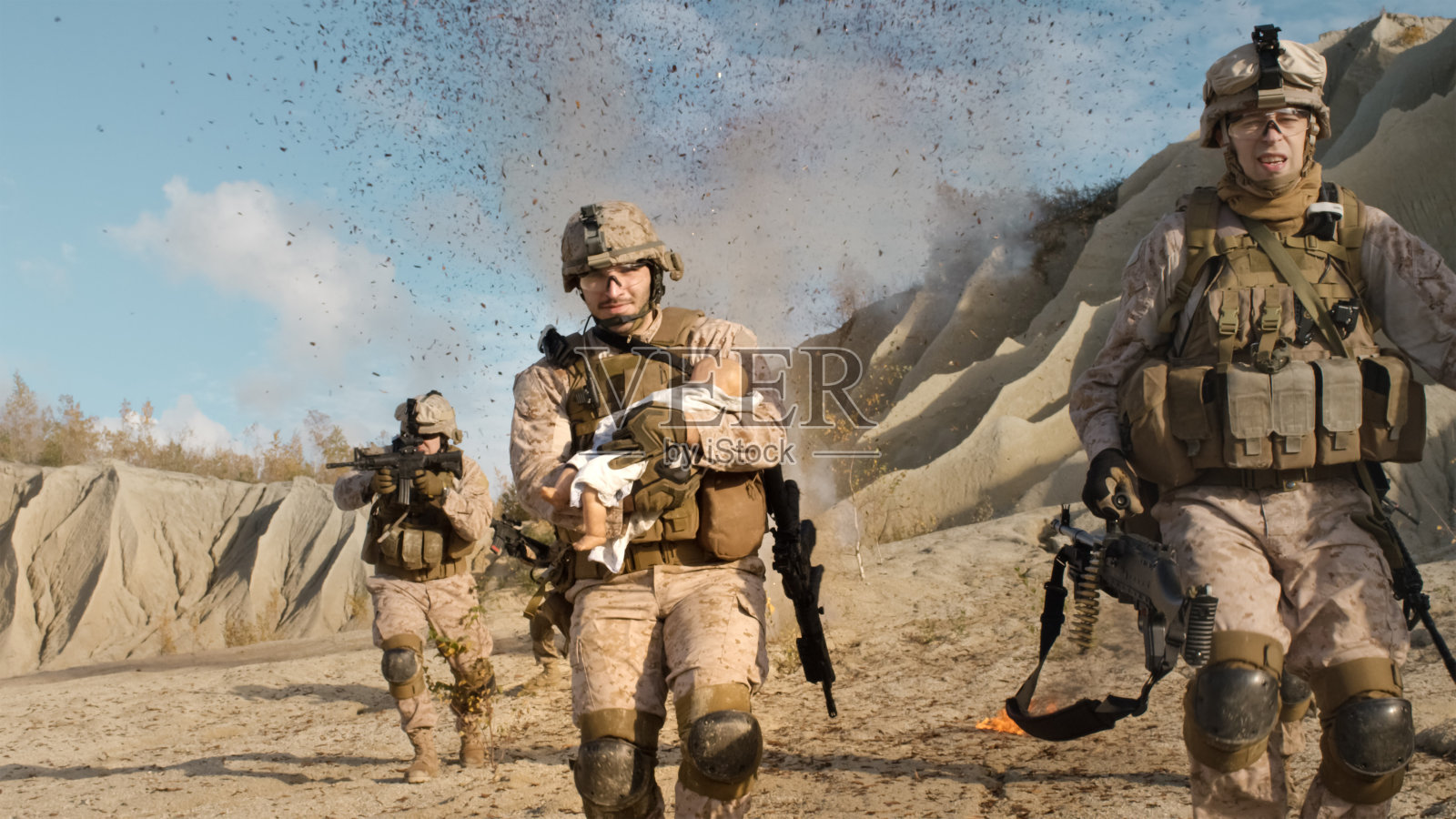 士兵抱着婴儿从后面的爆炸中逃跑。而其他成员在沙漠战斗掩护他们。照片摄影图片
