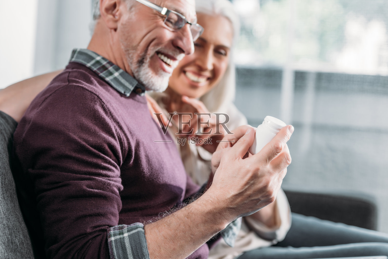 笑眯眯的老夫妇拿着药瓶坐在家里的沙发上照片摄影图片