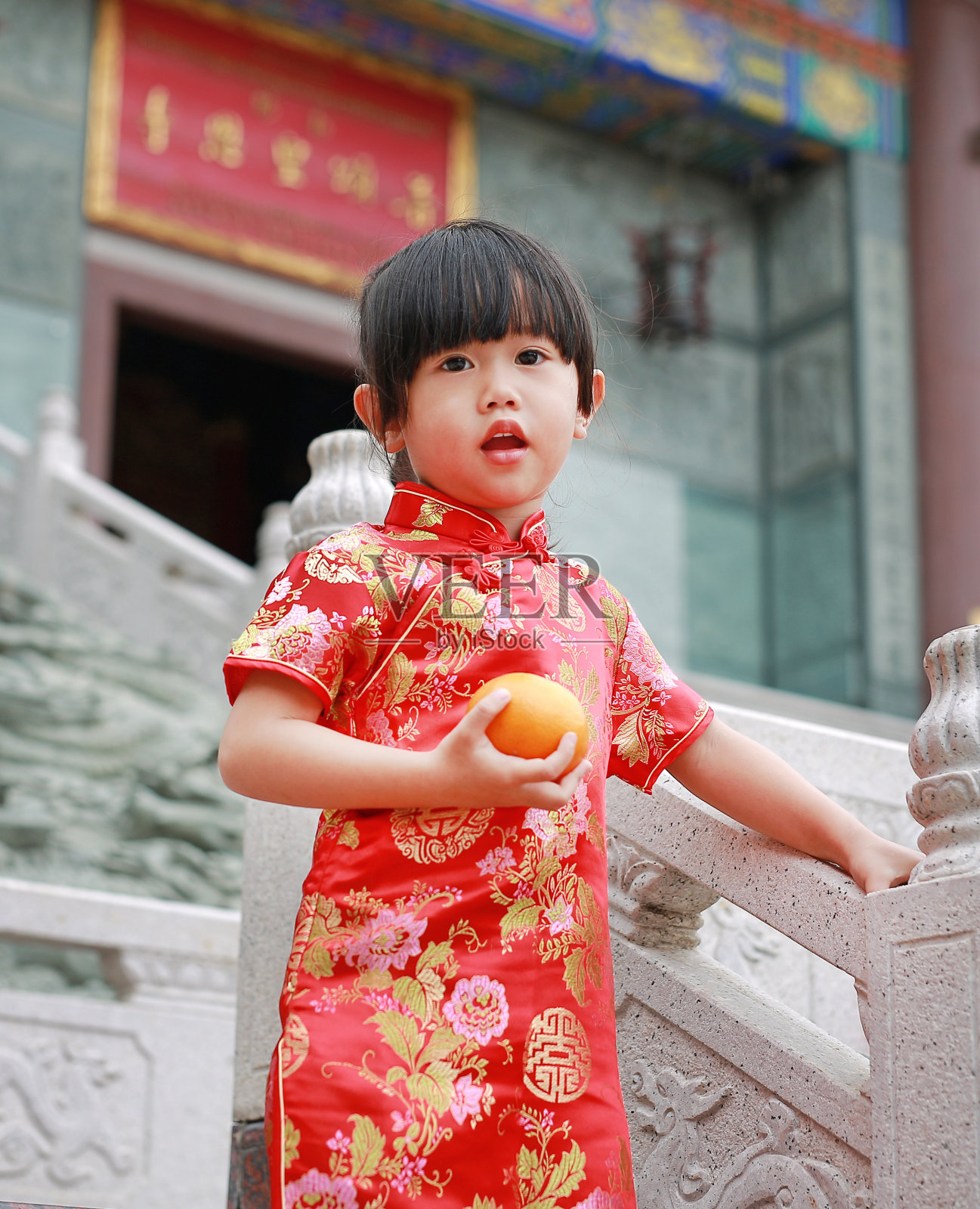 可爱的亚洲小女孩穿着传统的中国服装，拿着神圣的橙色。照片摄影图片
