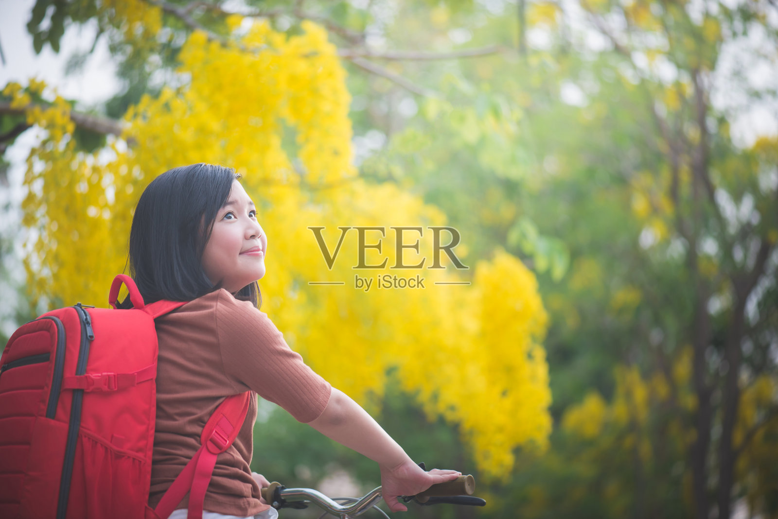 美丽的亚洲女孩与红色背包骑自行车在公园，泰国旅游概念照片摄影图片