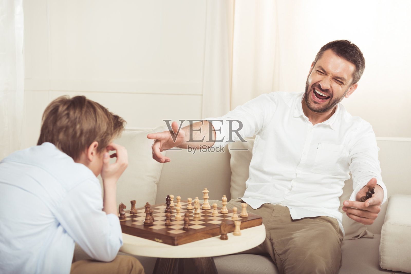 男子庆祝在象棋比赛中获胜，并指着不安的儿子在附近照片摄影图片