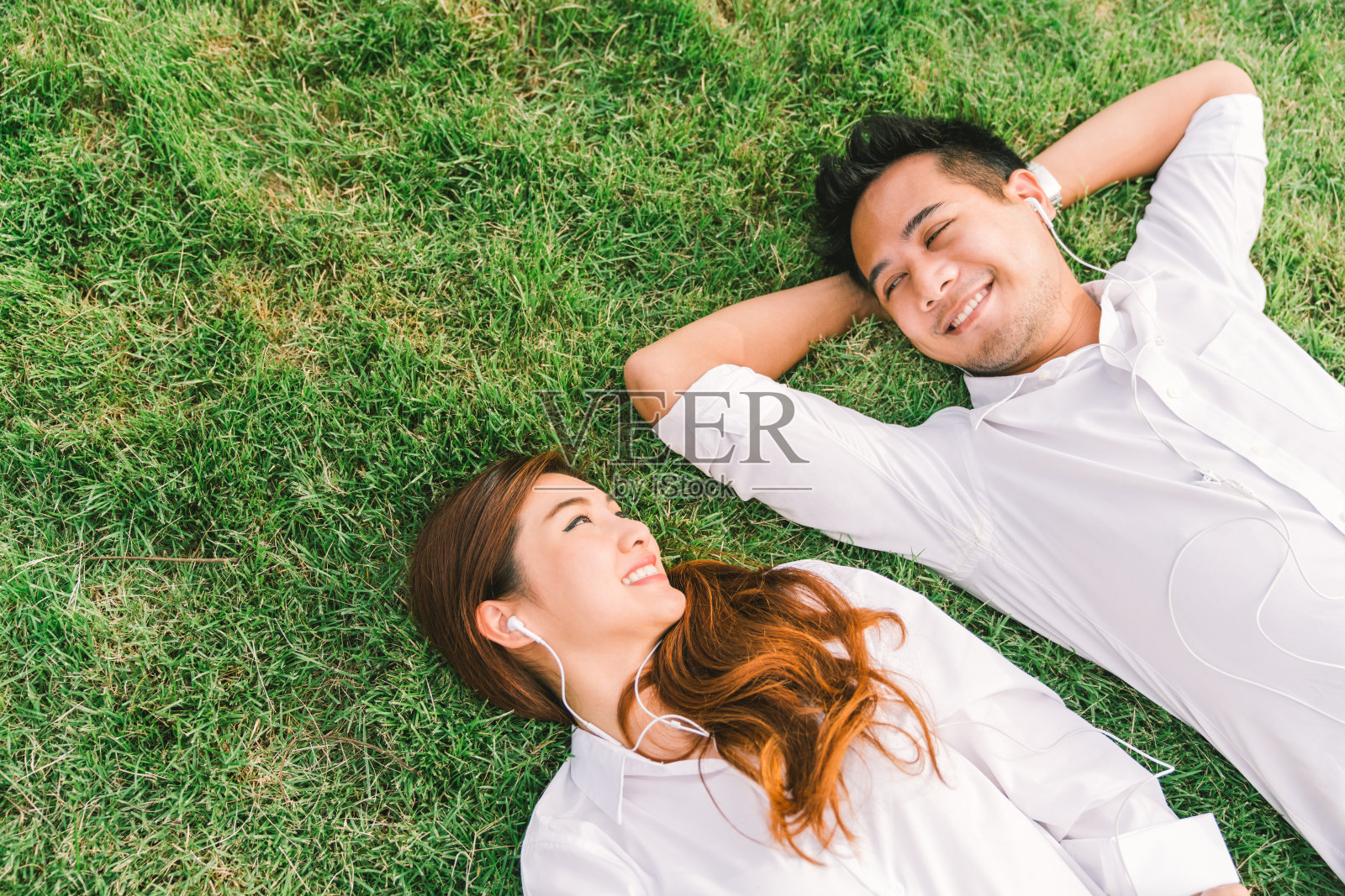 年轻的亚洲可爱的情侣或大学生一起躺在草地上，听着音乐，顶视图与抄写空间。爱情，关系，婚礼，或放松休闲的生活方式概念照片摄影图片