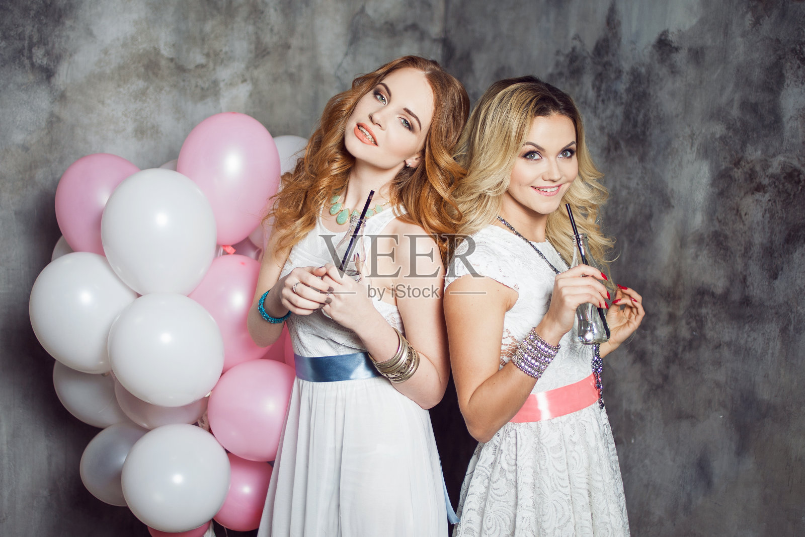 金发和红头发。两个年轻迷人的女朋友在派对上拿着气球。在灰色纹理背景照片摄影图片