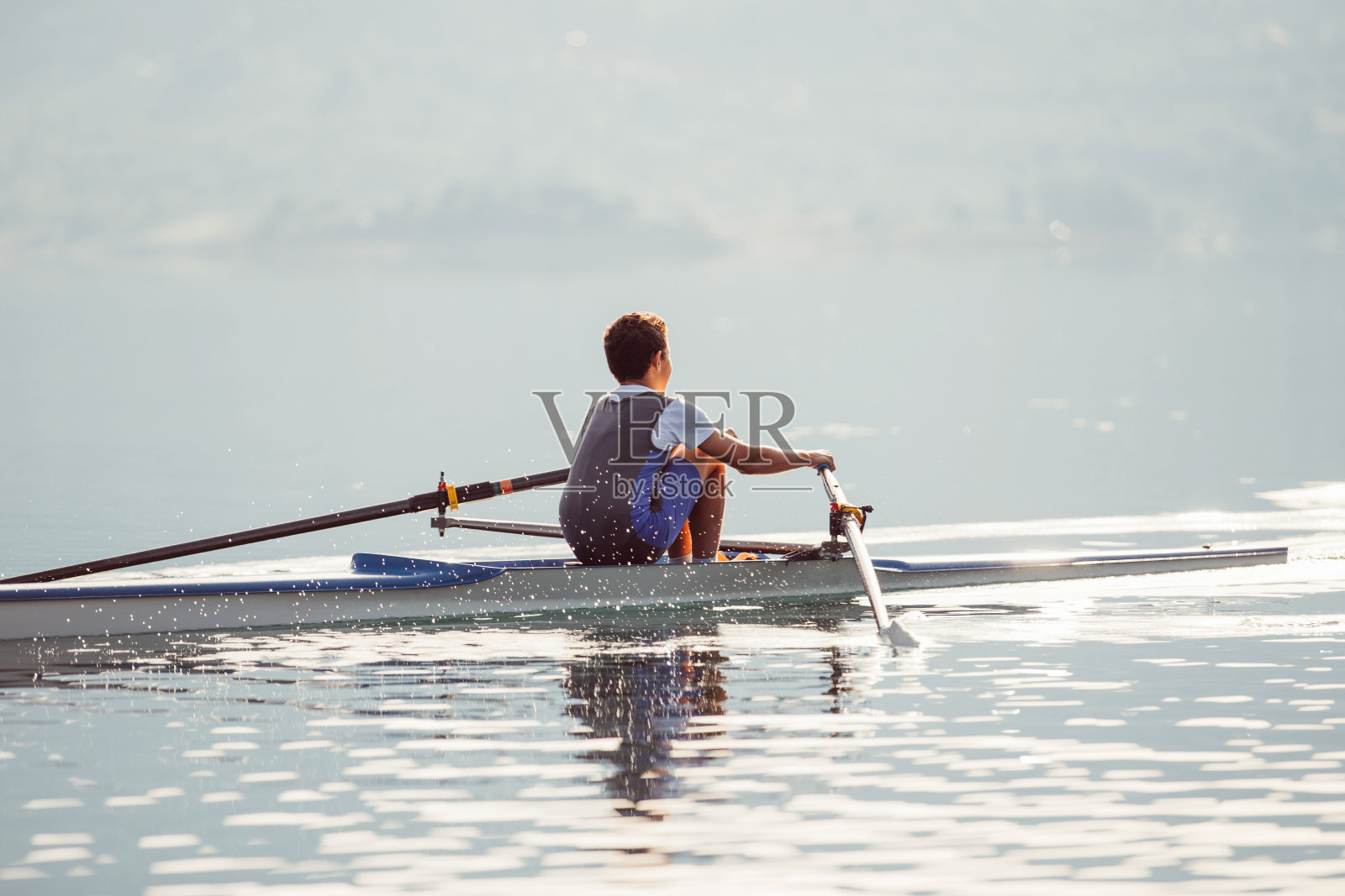 一位年轻的单人赛艇选手在宁静的湖面上划桨照片摄影图片