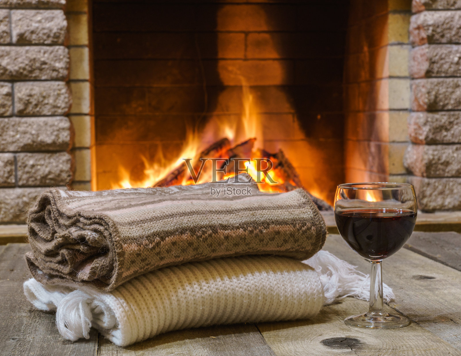 两杯红酒和羊毛织品，放在舒适的壁炉旁。照片摄影图片