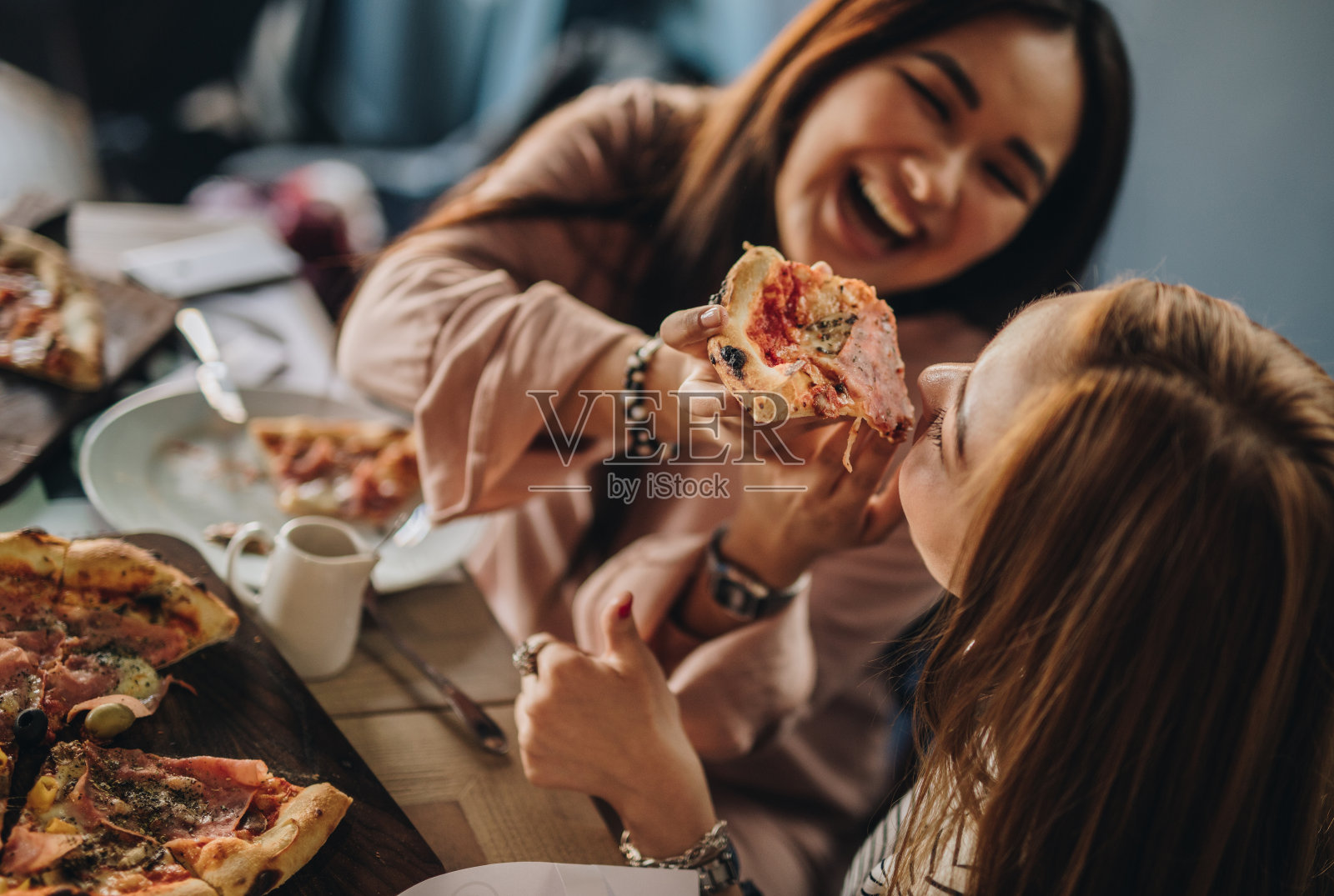 快乐的韩国女人吃披萨和有乐趣的餐厅。照片摄影图片