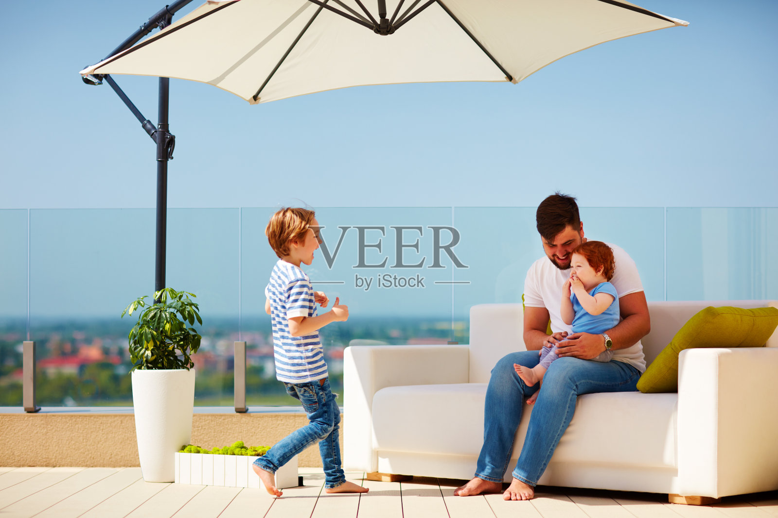 在温暖阳光明媚的日子里，一家人在屋顶露台的沙发上放松照片摄影图片