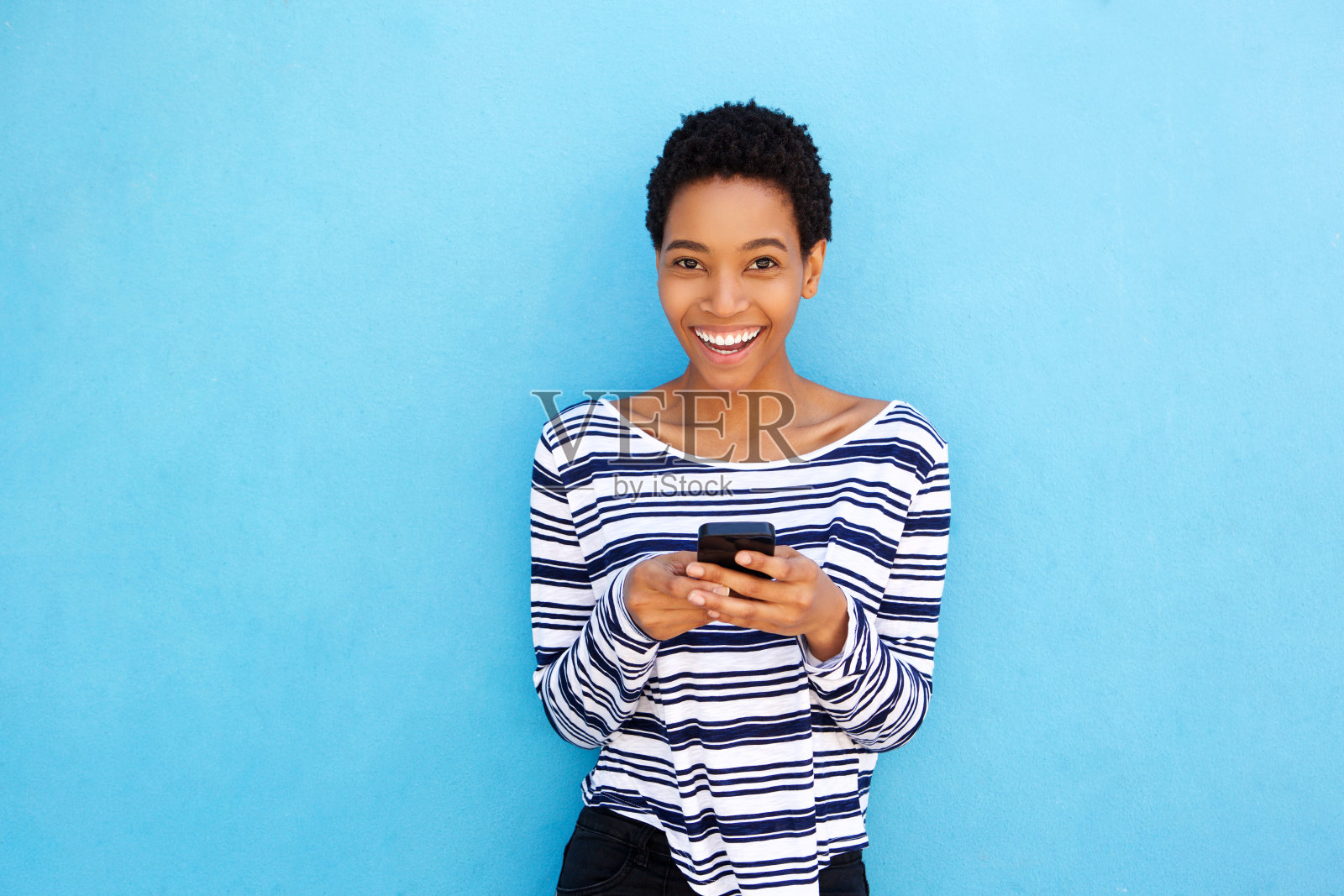 微笑的年轻黑人妇女拿着蓝色背景的手机照片摄影图片