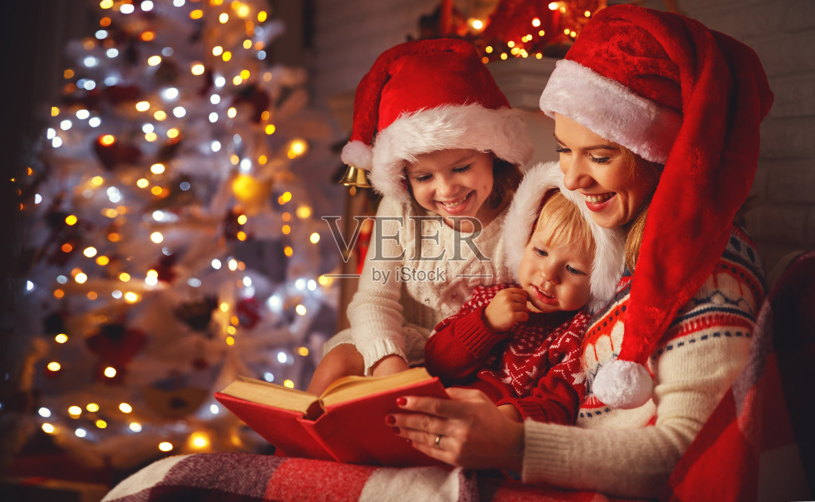 圣诞节时，家里的母亲和孩子们在壁炉旁看书照片摄影图片