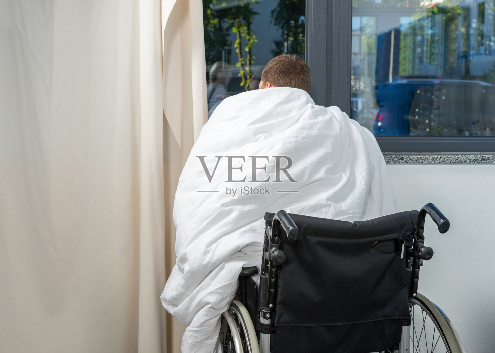 病房里靠窗坐着轮椅上盖着被子的病人照片摄影图片