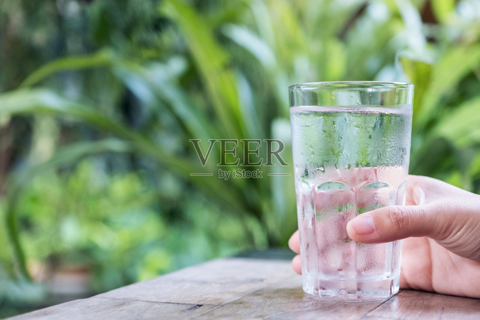 一只手拿着一杯冷水在绿色自然背景的木制桌子上的特写图像照片摄影图片