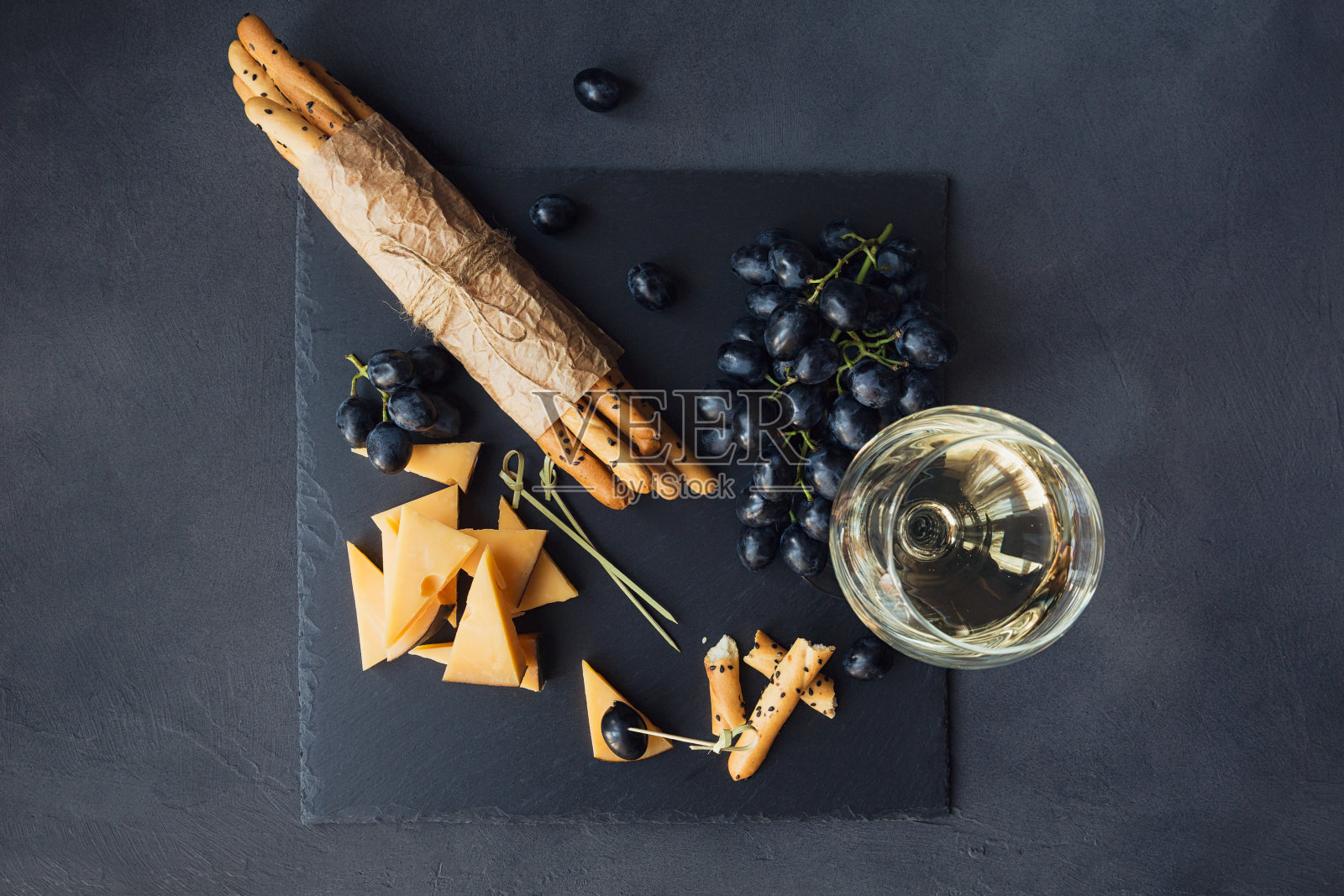 奶酪盘，饼干，葡萄和一杯白葡萄酒在深色的背景。照片摄影图片