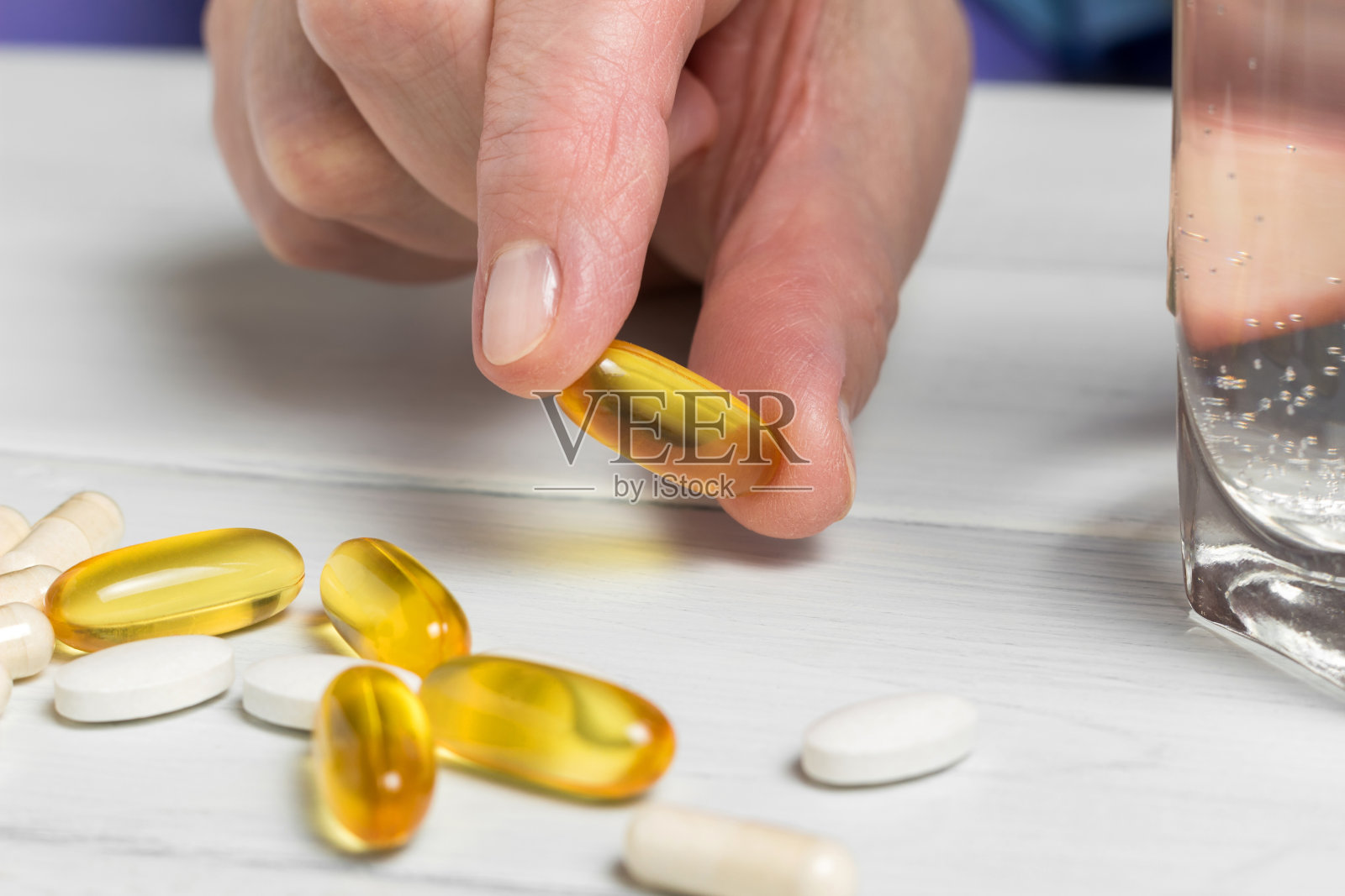 女人双手拿着黄色的omega - 3胶囊，白色的钙片，葡萄糖胺补充剂，一杯水放在木板桌上照片摄影图片