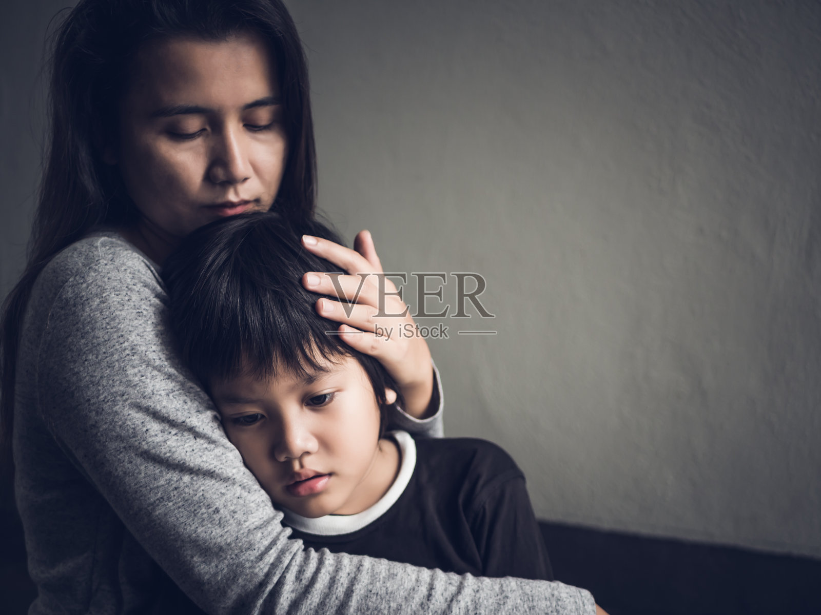 可怜的小男孩被妈妈抱在家里。父母、爱和团聚的概念。照片摄影图片