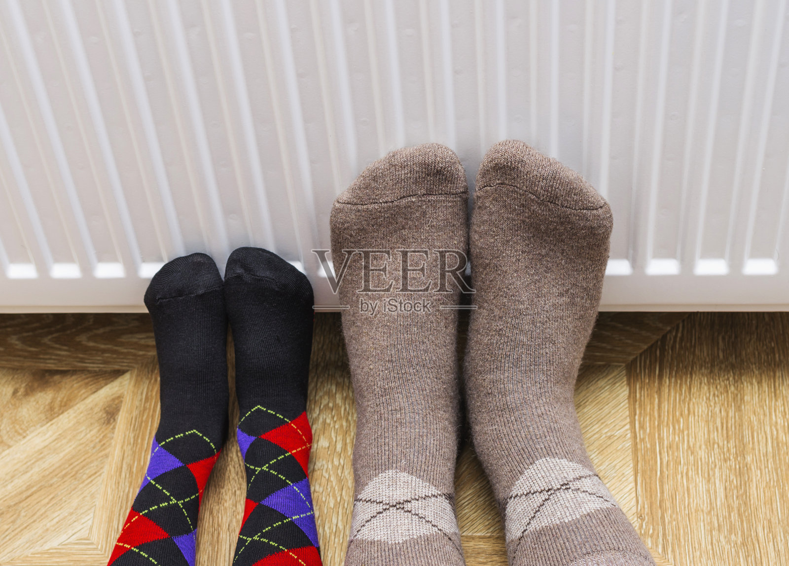 父子俩穿着冬天的羊毛袜子，在暖气片旁暖脚。照片摄影图片