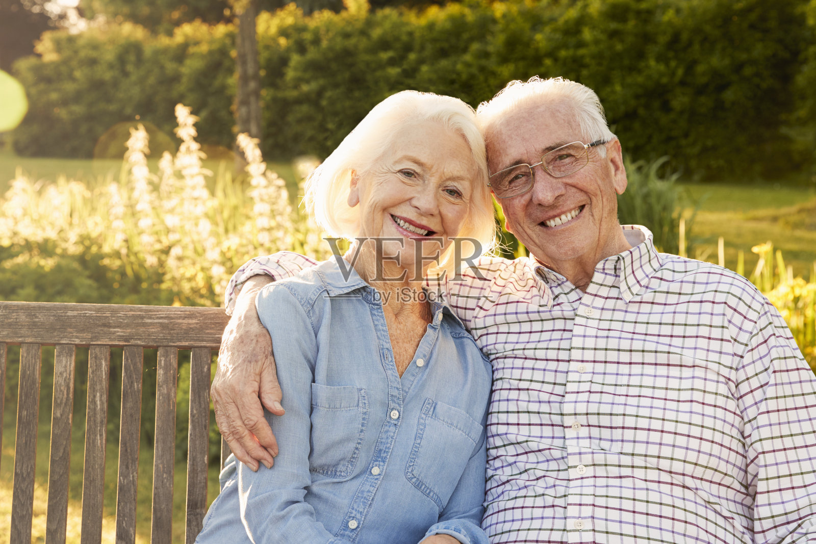 傍晚阳光下，一对老年夫妇坐在花园长凳上照片摄影图片