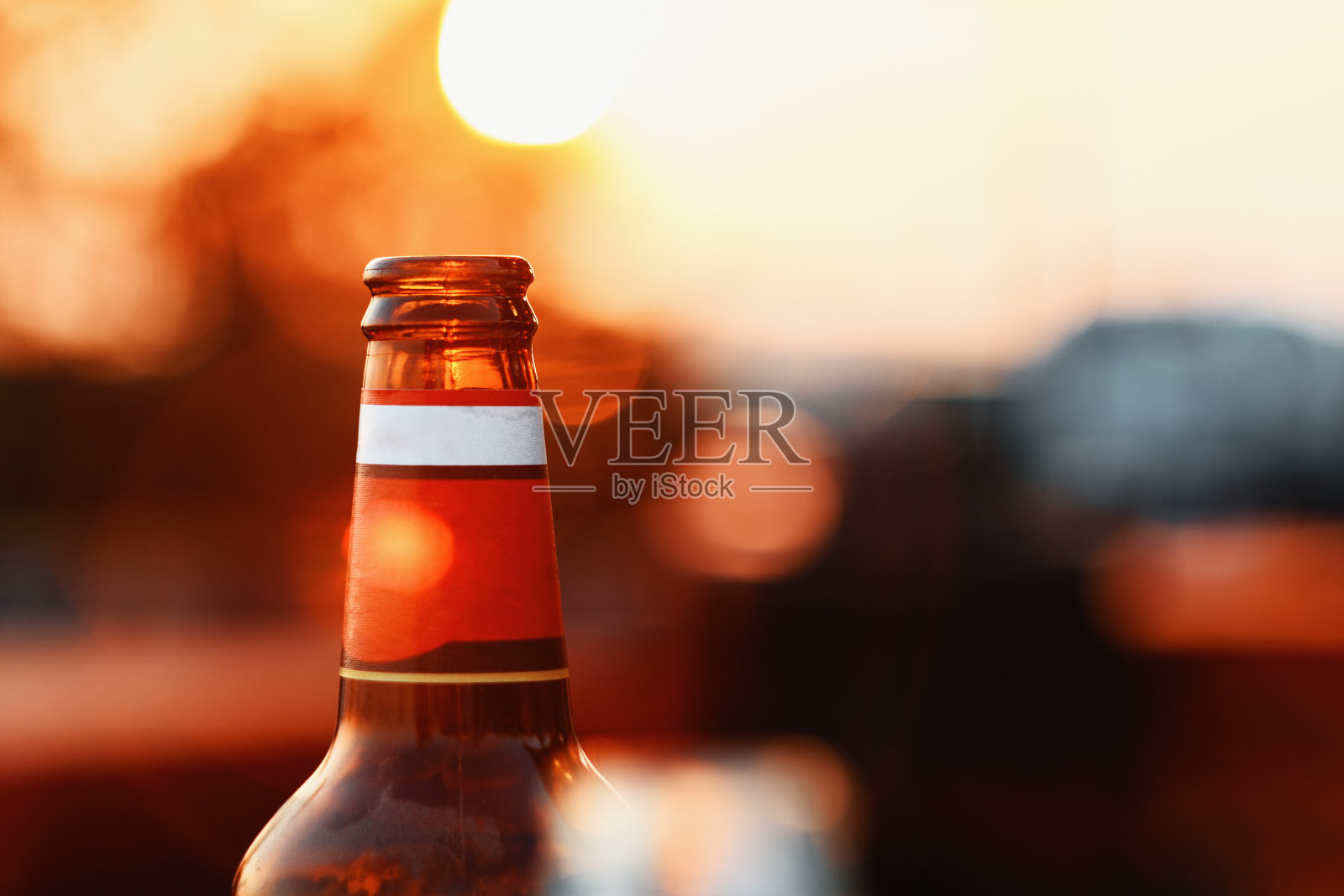 在模糊的背景和镜头光晕上，啤酒瓶对夏天的天空日落照片摄影图片