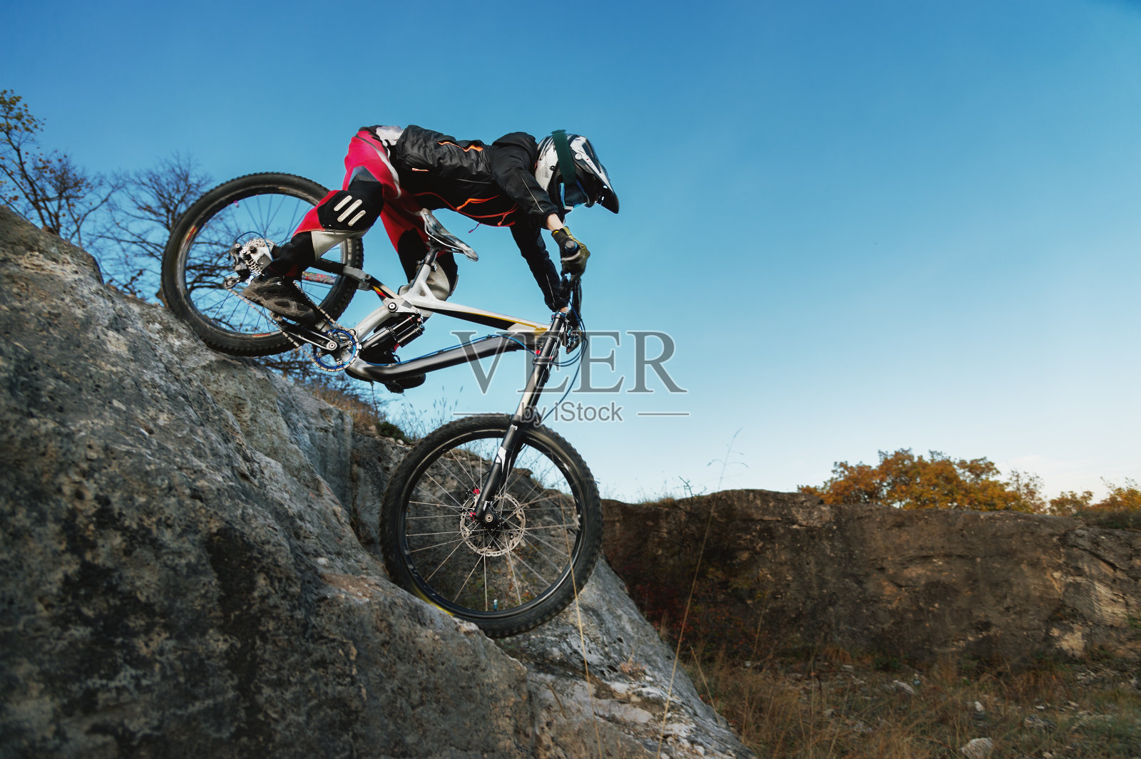 年轻的骑手骑着山地自行车从悬崖上下来，对着蓝天照片摄影图片