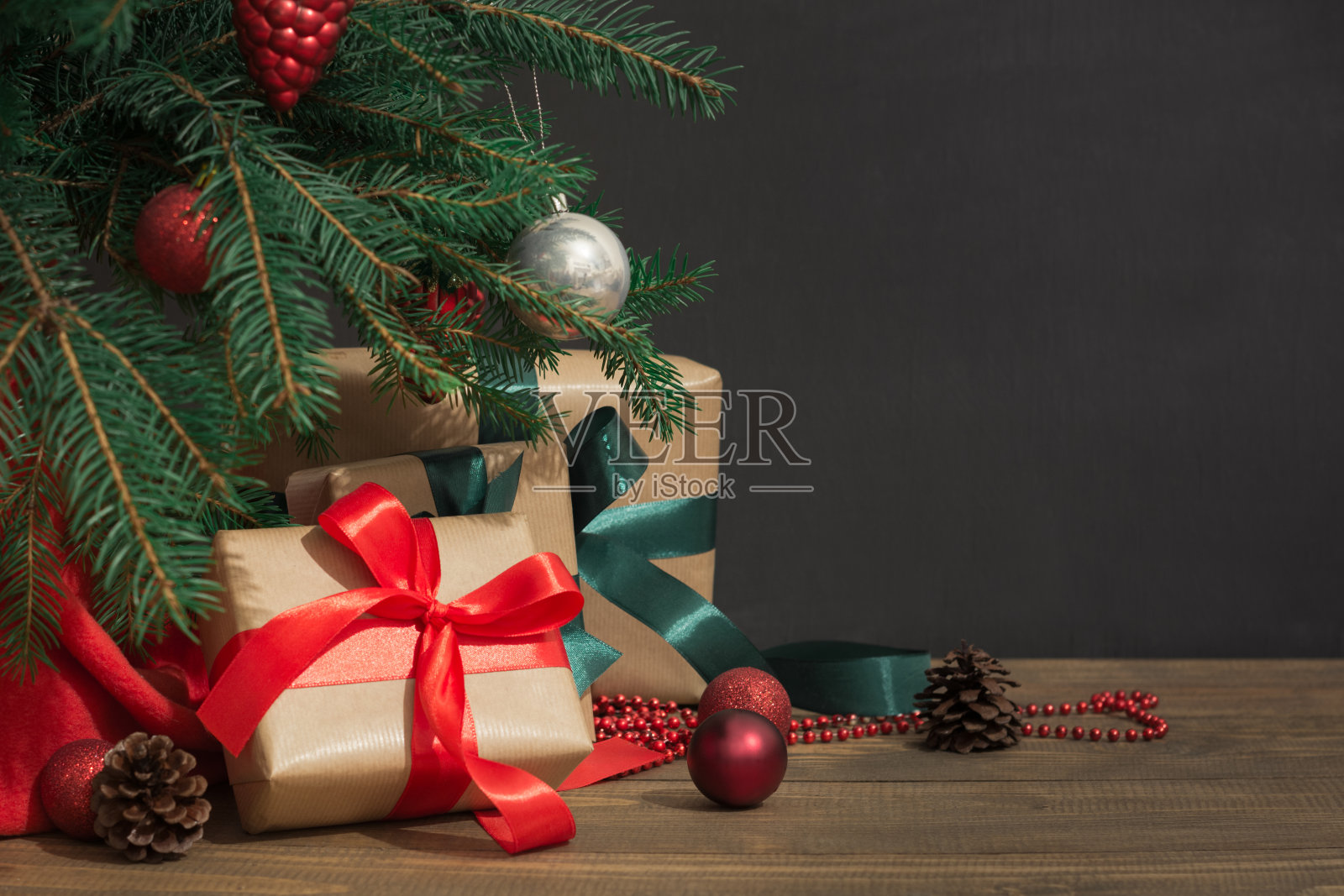圣诞节的背景。礼物用红丝带，圣诞老人的帽子和装饰在圣诞树下的木板上。照片摄影图片