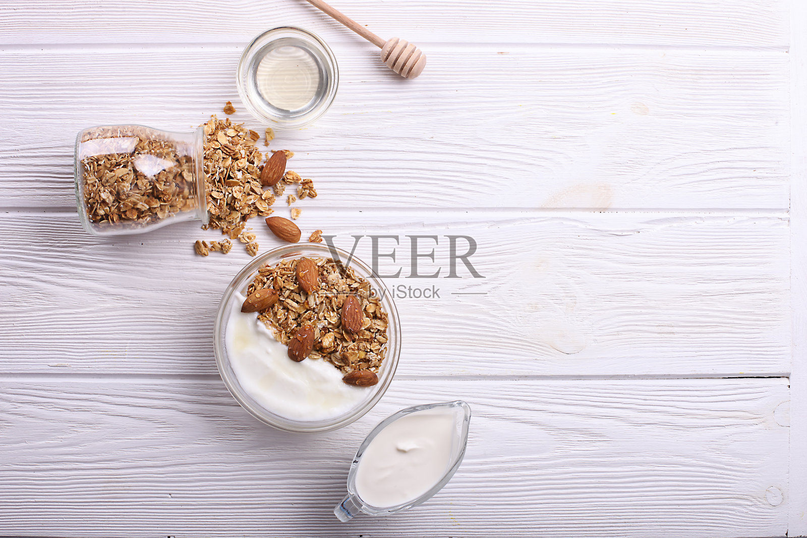 格兰诺拉麦片是一种超级食物，里面有杏仁和腰果，干果，葡萄干，玻璃碗里的樱桃，牛奶和希腊酸奶放在白色的木桌上，俯视图照片摄影图片