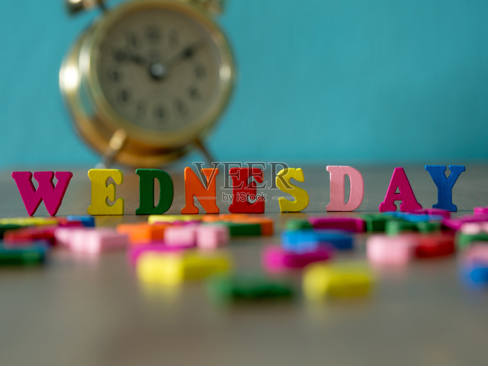 彩色木字星期三在木桌和古董闹钟和背景是粉蓝色。英文字母颜色由木制字母构成。照片摄影图片
